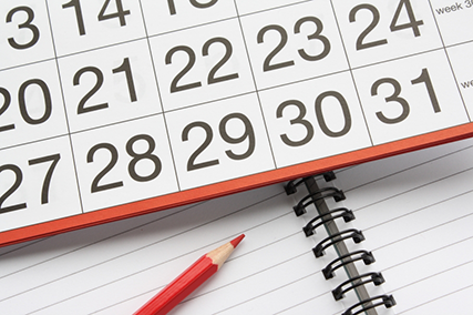 En kalender med datum och en röd penna placerade över ett skrivblock.