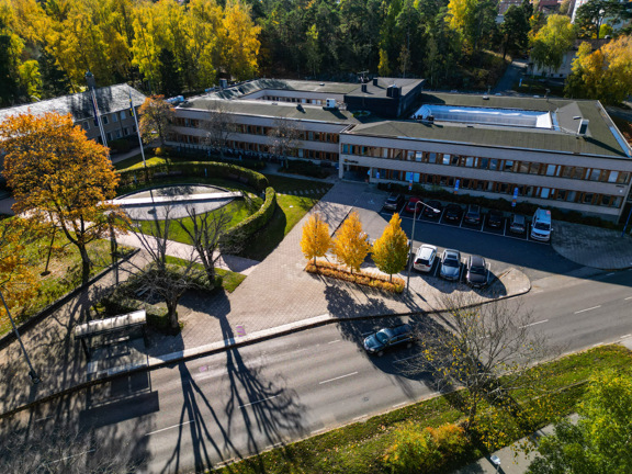 En drönarbild över Huddignes kommunhus. Man ser höstiga träd och kommunalvägen framför huset.